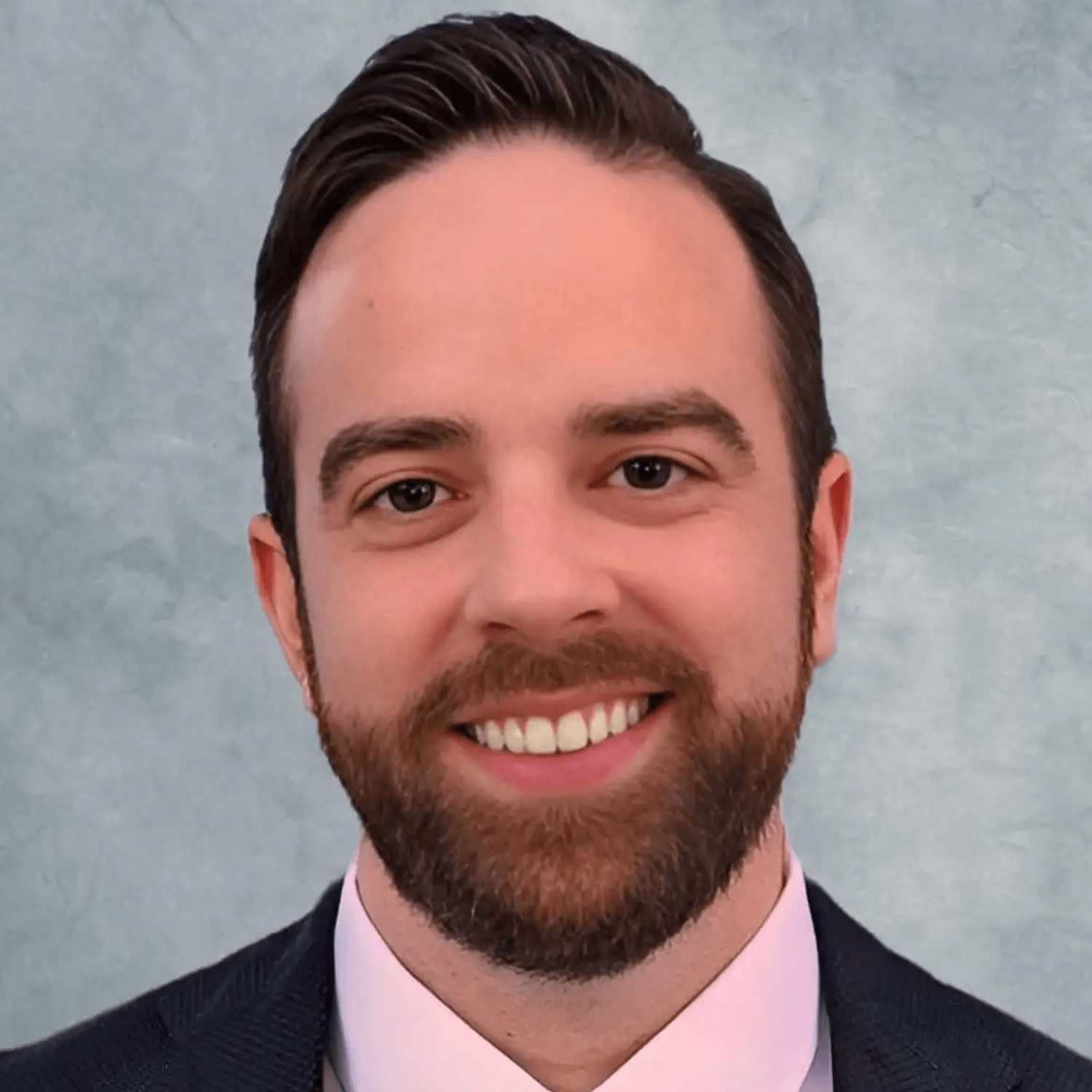 Headshot of Travis Furlan smiling, wearing a dark suit and pink shirt